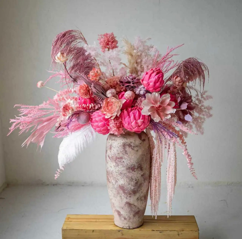 A bold preserved flower arrangement featuring pink protea, roses, and pampas in a handcrafted ceramic vase. Modern, elegant, and perfect for home décor or gifting.