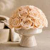 Floral Isle luxury champagne preserved roses arranged in an organic modern travertine stone vessel centerpiece, side view.