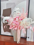 A luxury preserved flower arrangement featuring soft pink roses, pampas grass, white  feathers, asparagus myriocladuses, pink eucalyptuses and bunny tails grasses displayed in a glass ribbed vase.  Floral Isle brings a touch of sophistication and airy beauty to any living room, bedroom, or wedding décor.