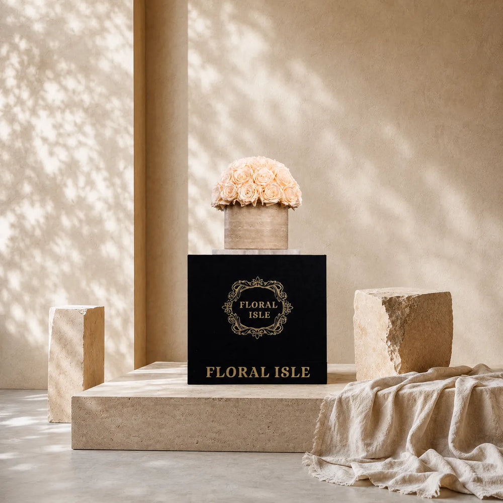 The champagne preserved roses stone arrangement sitting atop its luxury black Floral Isle gift box with a golden logo.